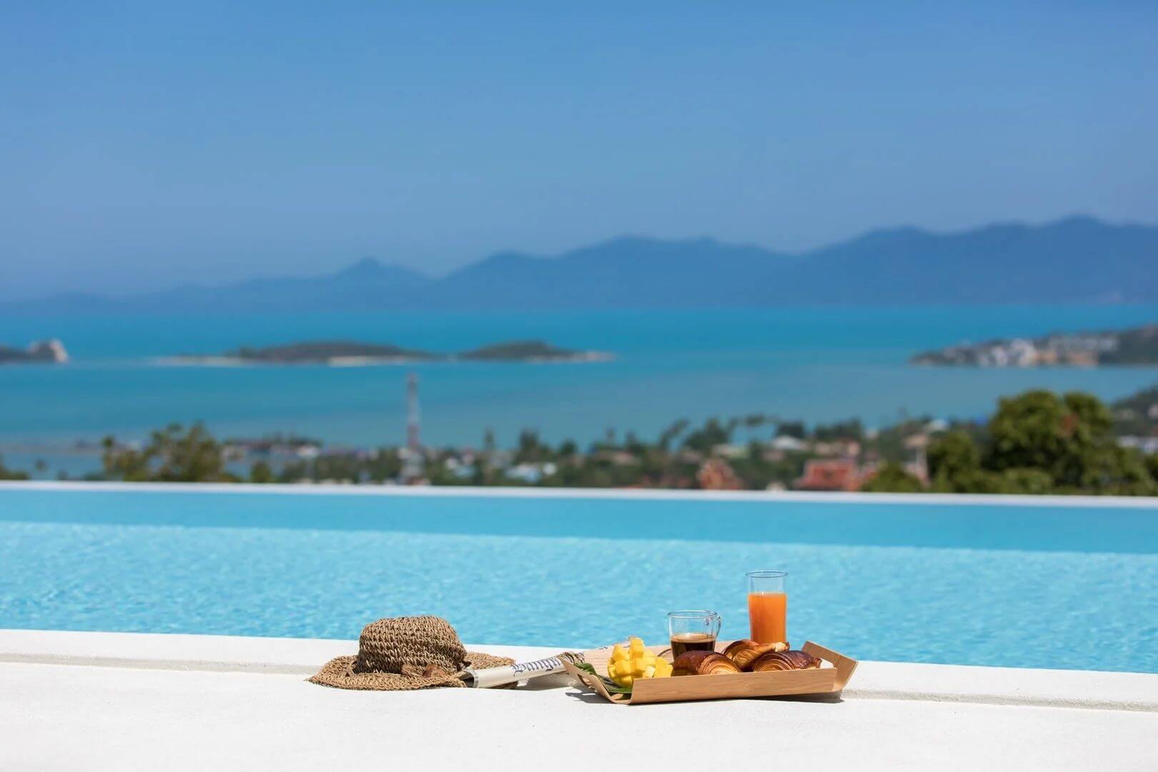 A breakfast tray of croissants, mango and juice on the pool edge above the bay.