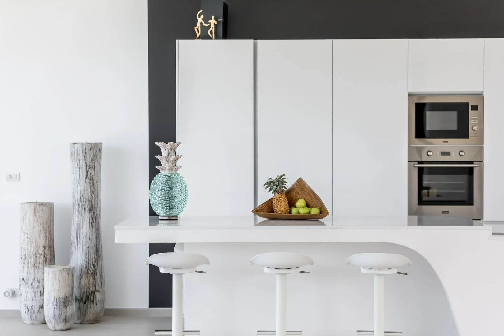 The white gourmet kitchen — bar stools, double oven, fruit on the counter.
