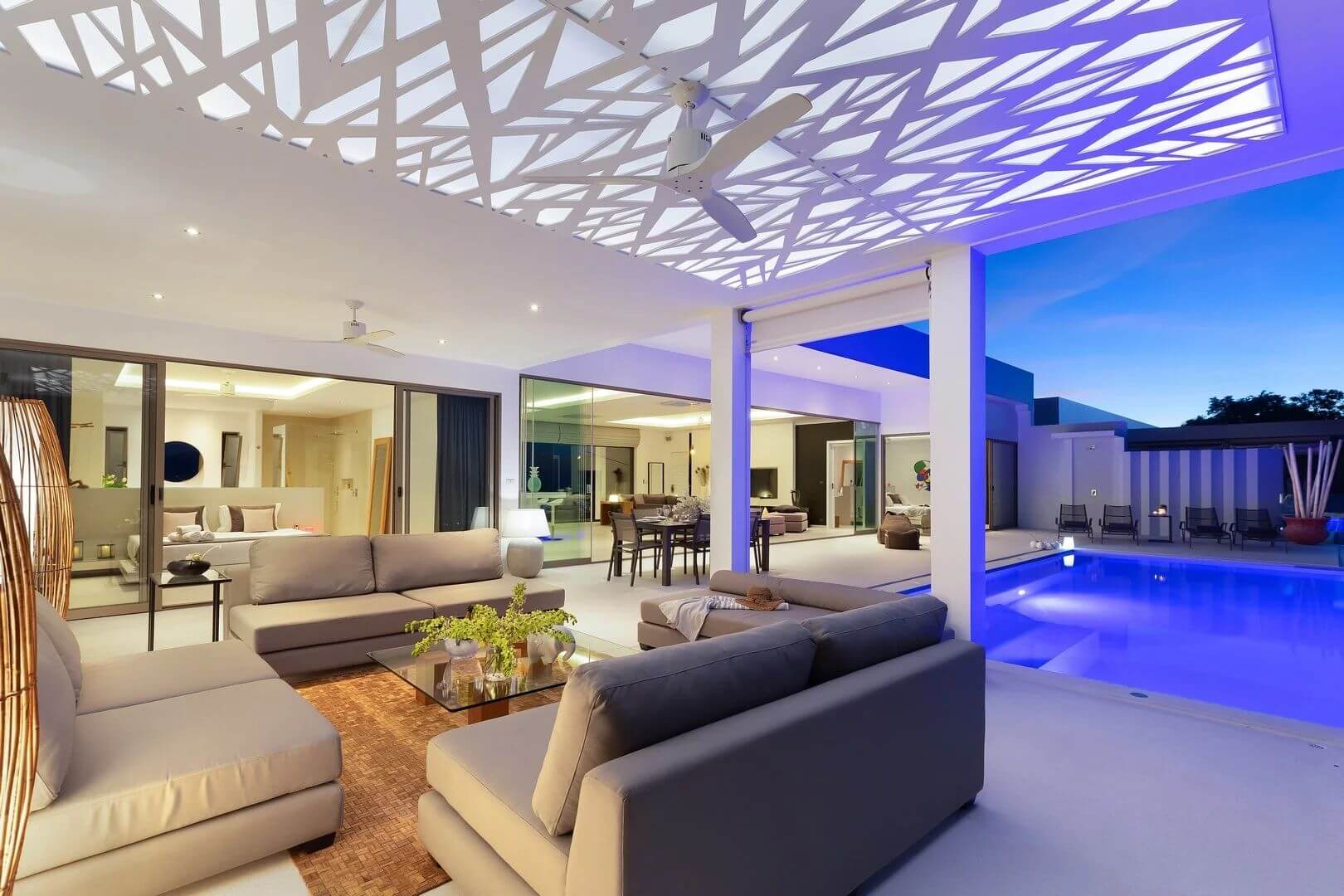 Night view across the outdoor lounge into the lit interior and pool.