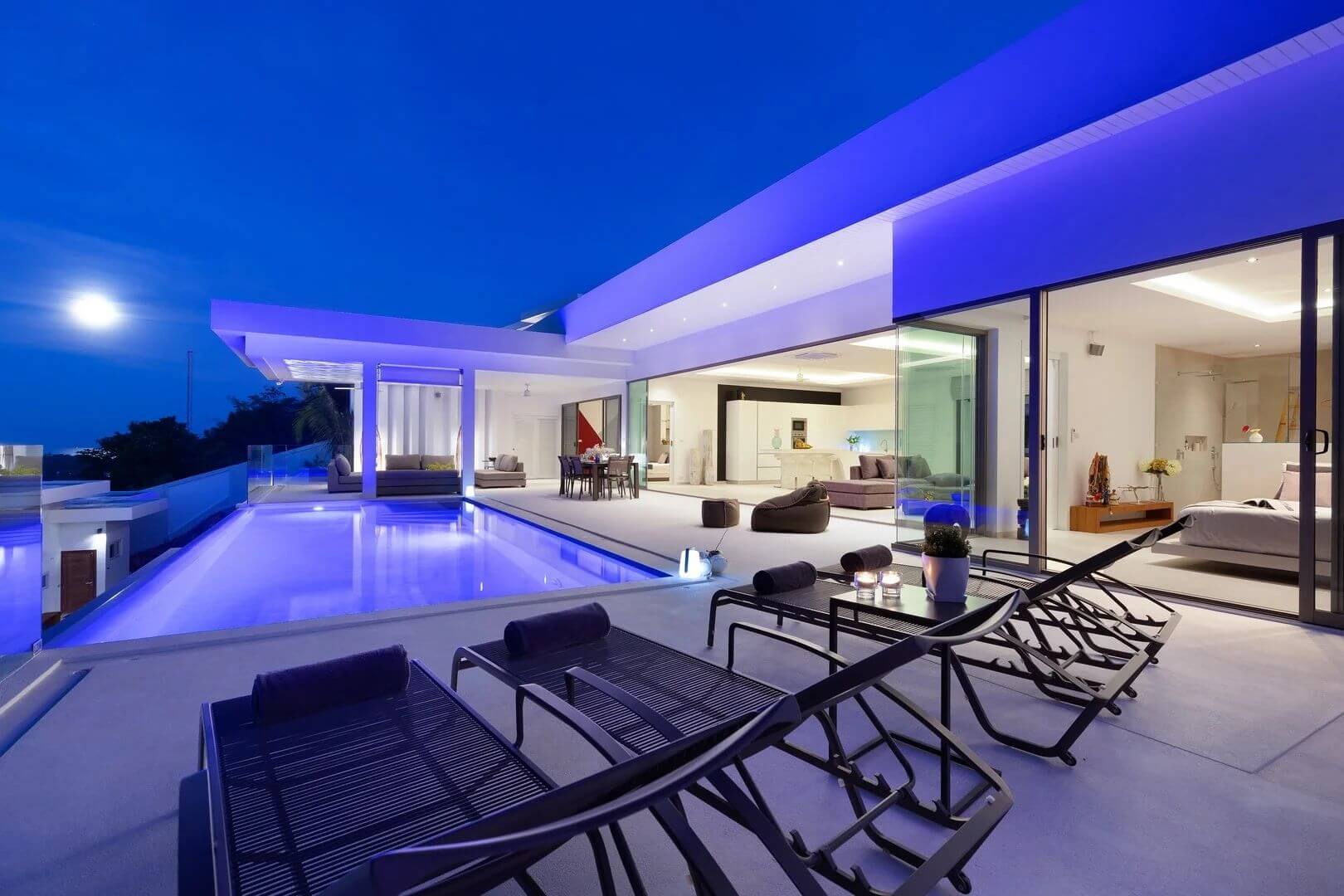 The villa at night under a full moon — pool glowing, every room lit and open.