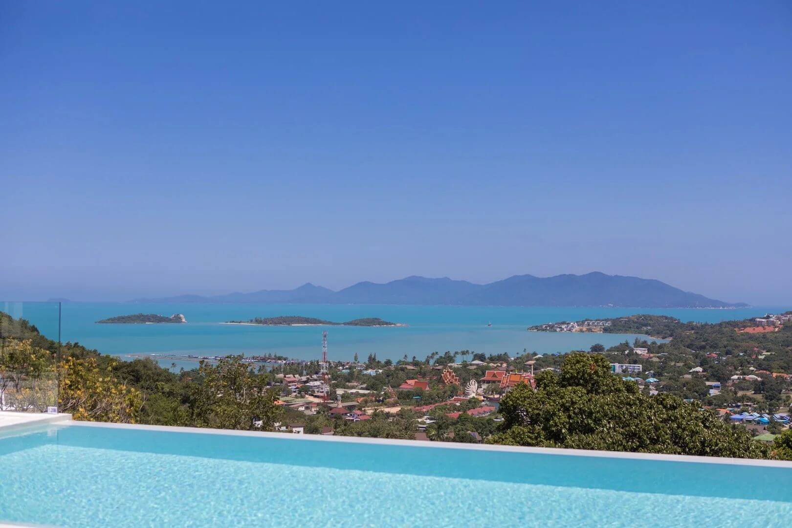 The daytime view from the pool — Wat Plai Laem below, the bay and its islets, Koh Phangan across the water.