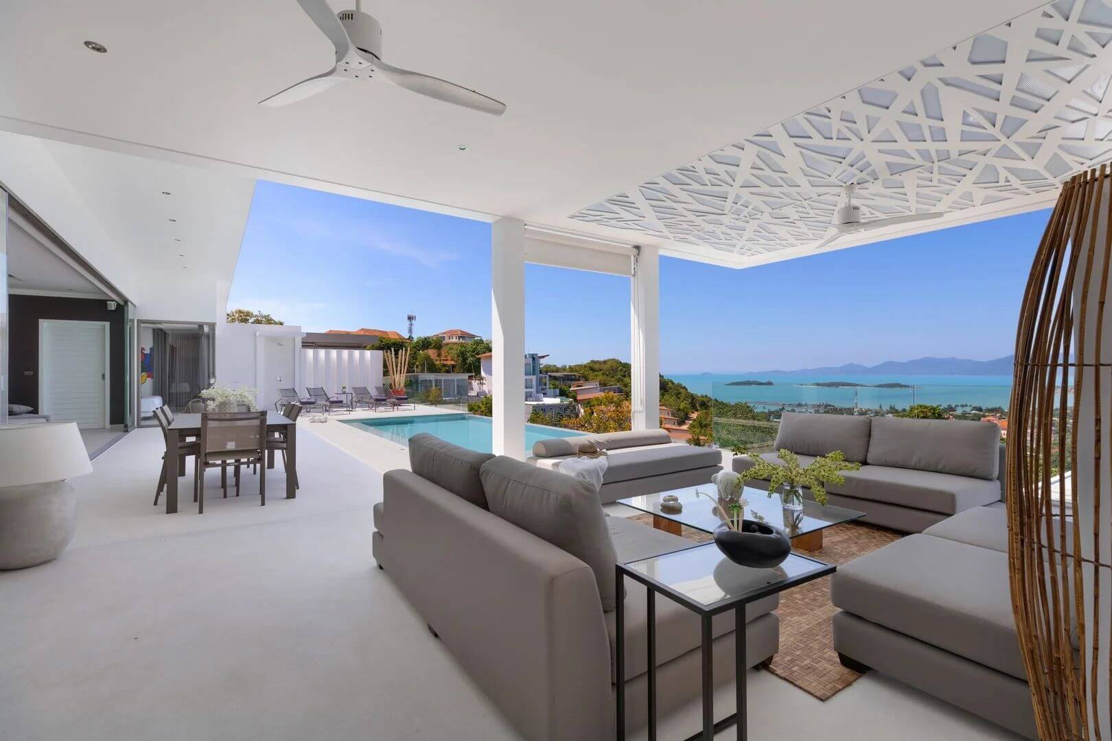 Noon under the sala — lounge seating and the dining table open to the pool, the bay and the islands beyond.