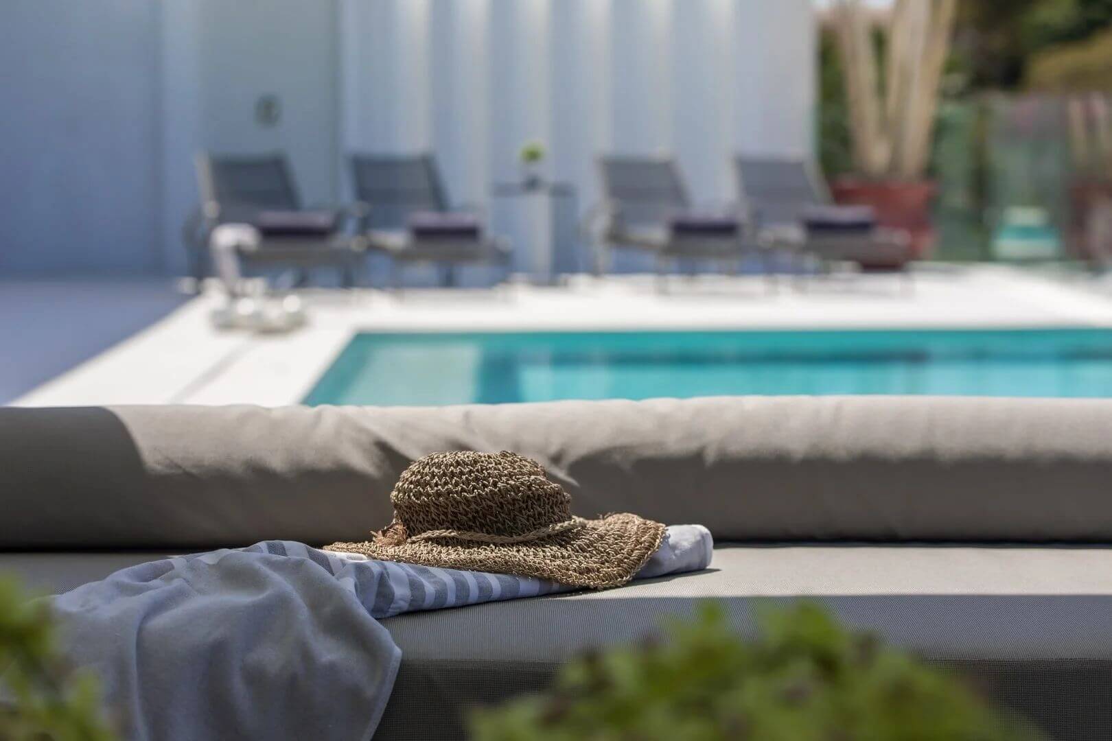 A straw hat and towel resting on a daybed by the pool.
