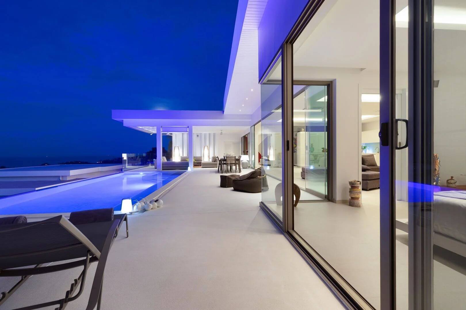 The terrace at blue hour — pool lit, bedrooms glowing, sea in the dark.