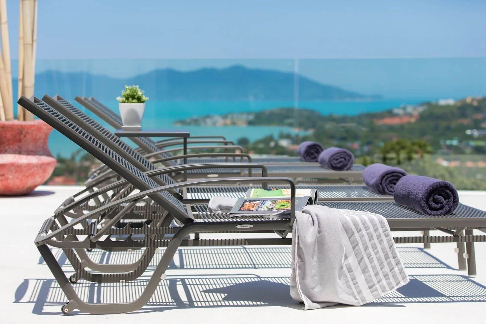 Rolled towels on loungers, the bay and its green islets out of focus beyond.